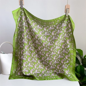 Close-up of green paisley silk scarf with SUN border hanging on wooden clips