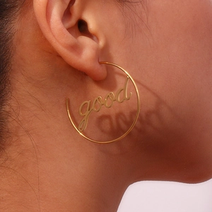Detailed view of large gold hoop earring with 'good' script lettering on a model