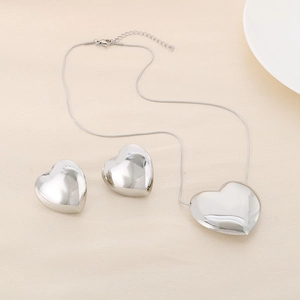 Parure de bijoux cœur en argent poli avec collier et boucles sur tissu beige texturé