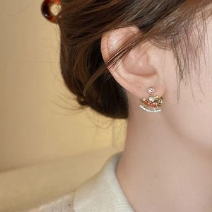 Golden rocking horse earrings with transparent diamonds worn by a model in soft light