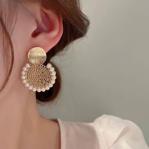 Dettaglio di orecchini d'oro con dischi spazzolati e perle indossati da una modella