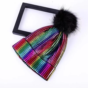 Colorful metallic knit beanie with a large faux fur pompom on a clean white background