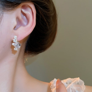 Detailed view of silver stud earrings with zircon crystals and pearls worn on ear