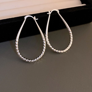 Detailed view of silver teardrop hoop earrings with faceted texture on a black display box