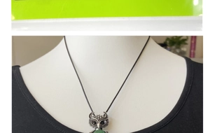Detail of owl pendant with green gemstone inlay and antique silver feather texture