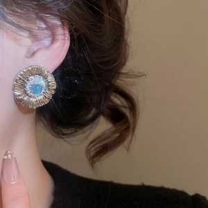 Close-up of flower stud earring with light blue stone and zircon on a model's ear