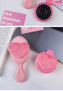 Close-up of pink heart-shaped plush hairbrush and compact mirror on white desk