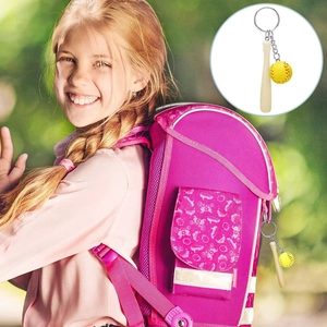 Close-up of mini baseball bat and softball keychain hanging on a pink backpack zipper