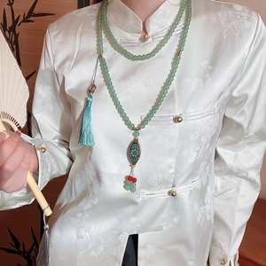 Detailed close-up of green crystal beaded necklace with blue tassel on silk garment