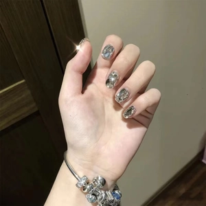 Detail of luxury press-on nails with silver rhinestones and a multi-pendant metal bracelet