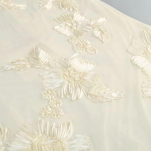 Detailed close-up of premium cream mesh fabric with 3D ribbon flower embroidery