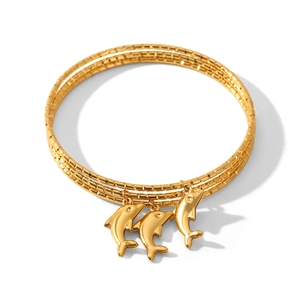 Detailaufnahme von drei goldenen dreilagigen Armreifen mit feinen Delphin-Anhängern