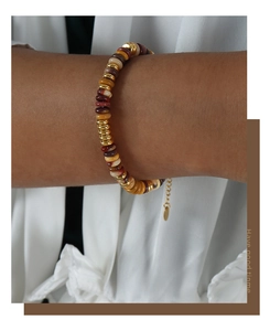 Detail eines handgefertigten Natursteinarmbandes mit goldenen Perlen und Logo-Anhänger