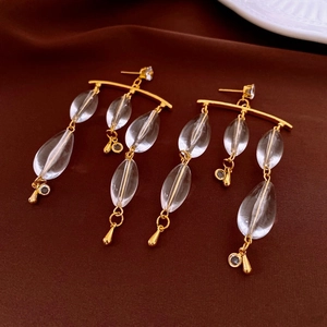 Detailed close-up of long tassel earrings with clear teardrop beads on a brown fabric