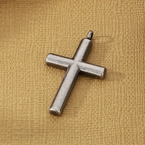 Detail of vintage silver stainless steel cross pendant with aged finish on yellow paper