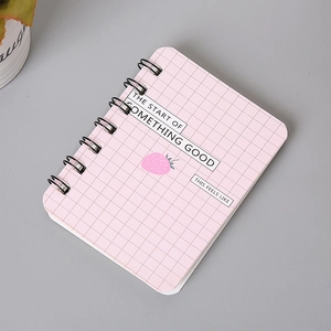Close-up of pink grid A7 spiral notebook with strawberry design on a grey desk