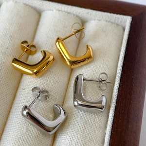 Macro shot of minimalist gold and silver U-shaped chunky stud earrings in a jewelry box