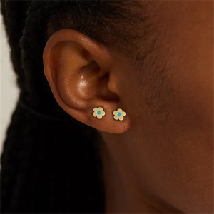 Close-up of golden flower stud earrings with blue center stone worn by a model