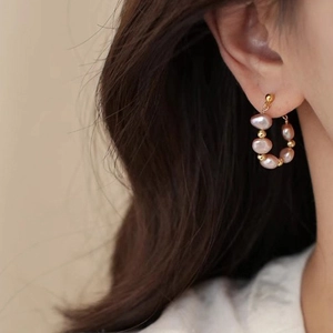 Detail of beaded hoop earring featuring pink baroque pearls and golden beads on model