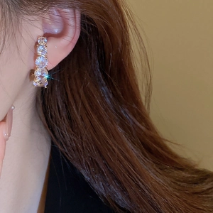 Close-up of model wearing curved gold plated earrings with graduated white cubic zirconia