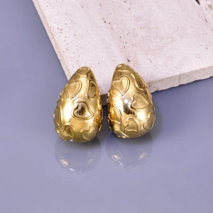 Close-up of golden teardrop earrings with embossed heart pattern on a reflective surface
