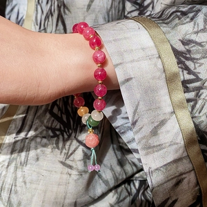 Detail of beaded bracelet with pink lotus charm and gold spacers on silk sleeve