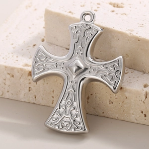 Silver stainless steel cross pendant with embossed pattern on natural stone display