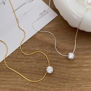 Minimalist gold and silver cubic zirconia pendant necklace set on a rustic wood surface