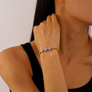 Détail d'un bracelet à perles dorées avec trèfles argentés porté au poignet féminin