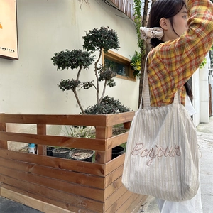 Detail of striped canvas tote bag with Bonjour embroidery in a casual outdoor setting