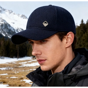 Detailaufnahme einer dunkelblauen Winter-Baseballkappe mit Metal-Logo im Schneegebirge