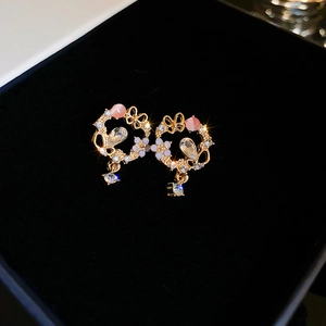 Detail of floral earrings with pink cat eye stone, zircons and golden bow on velvet