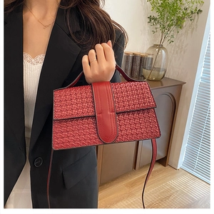 Detail of red woven texture shoulder bag worn by model in a cozy interior setting
