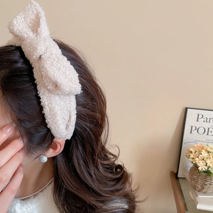 Detail of cream white plush bow headband in soft bouclé fabric worn by a model