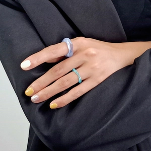 Close-up of light blue resin ring and thin beaded crystal ring on a model hand