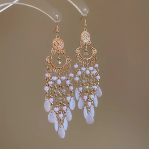 Detail view of ethnic gold tassel earrings with pink beads and white teardrop stones