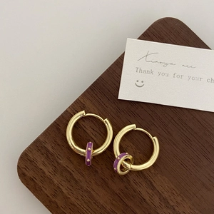 Detail of vintage gold earrings with purple enamel charms resting on a wooden display block