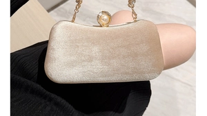 Detalle de bolso de fiesta en terciopelo champán con broche de perla y cadena