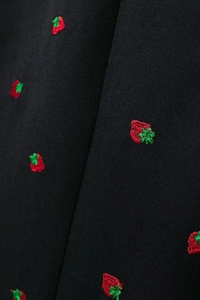 Gros plan de broderies fraises rouges avec feuilles vertes sur tissu tissé noir