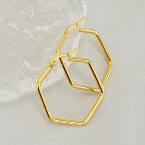 Polished gold hexagonal hoop earrings displayed on a glass block with soft lighting