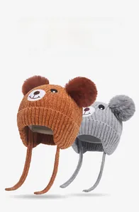 Detail of baby winter knit hats with bear embroidery and double faux fur pom-poms