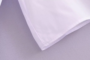Détail du bord de manche de chemise blanche montrant les coutures doubles et le tissu