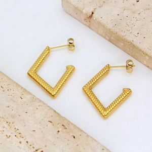 Close-up of golden geometric square earrings with textured spiral ribbing on stone pedestals