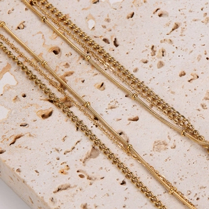 Detail of layered gold beaded and Cuban link chains resting on a textured stone