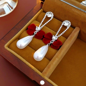 Detail of red velvet bow earrings with teardrop pearls and rhinestones in a wooden box