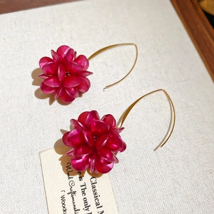 Dettaglio di orecchini a fiore rosso rosa con ganci dorati su tessuto bianco morbido