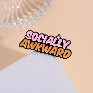 Enamel brooch with 'SOCIALLY AWKWARD' text in pink and orange on a white stand