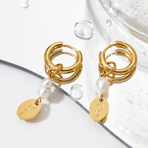 Detail of gold pearl earrings with a rose engraved pendant on a reflective water surface