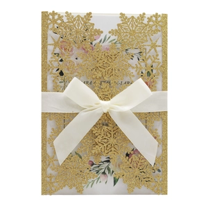 Close-up of glittery gold snowflake laser-cut wedding invitation with a white silk bow