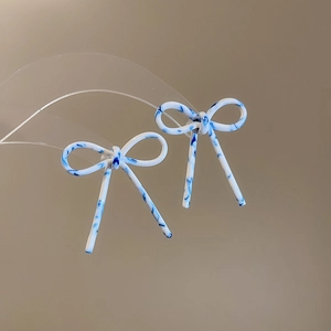Détail de boucles d'oreilles nœud en acétate avec texture marbrée bleue sur support clair
